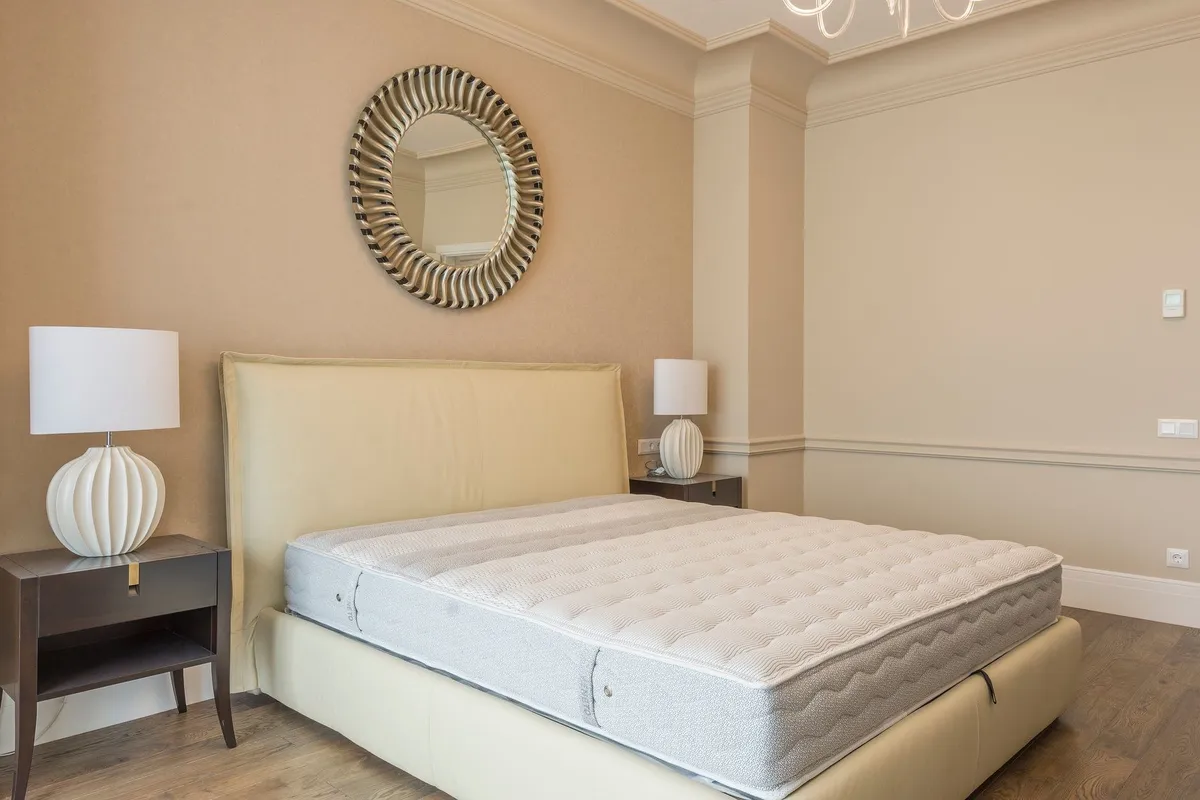 A spacious bedroom with modern decor, elegant lighting, and a plush neutral-toned bed, suggesting comfort.